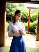 A woman in a white shirt and blue skirt standing in front of a window.