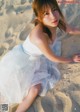 A woman in a white dress sitting on the sand.