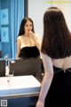 A woman in a black dress brushing her teeth in front of a mirror.