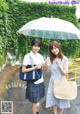 Two young women standing next to each other holding an umbrella.